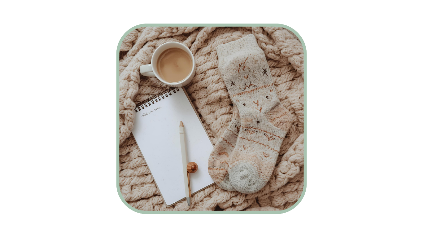 Notizbuch, eine Tasse Tee und gemusterte Wollsocken auf einer Strickdecke