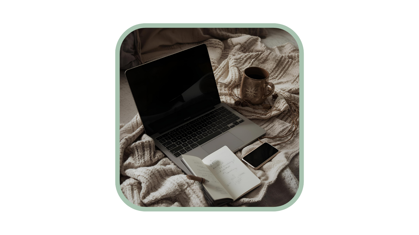 Laptop, handschriftliches Notizbuch, Smartphone und eine Tasse Tee auf einer Strickdecke